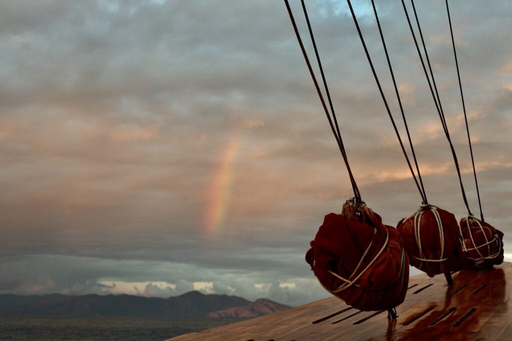 Rainbow at sunset behind the furled red sails of Tiger Blue