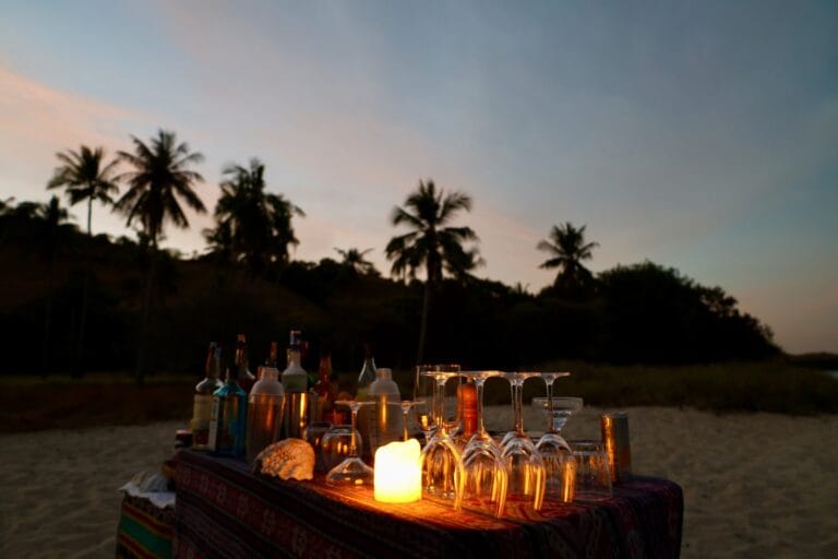 Candlelit beach bar with glasses under palm trees at dusk