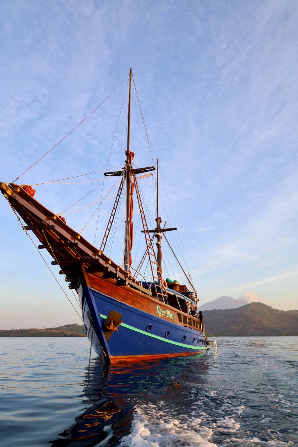 Tiger Blue 1 at anchor in golden evening light, with hills and a volcano behind