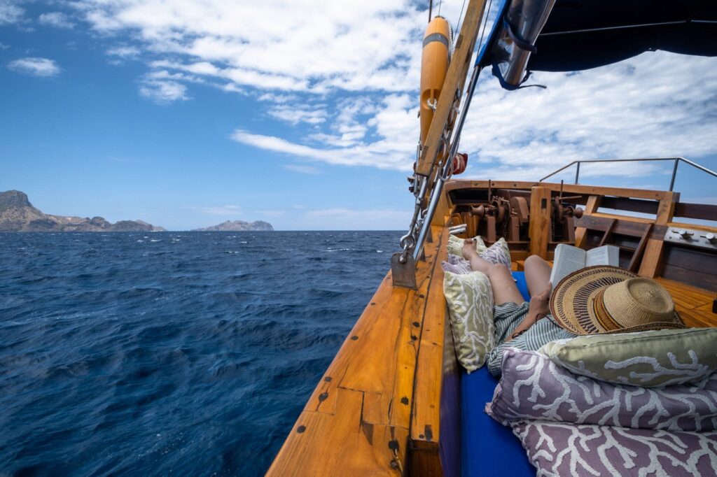 Guest reads on the cushioned bow lounger of Tiger Blue while sailing past Komodo islands