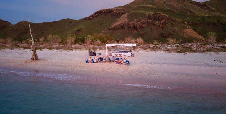 Drone view at dusk of Tiger Blue guests dining under a white canopy on the beach