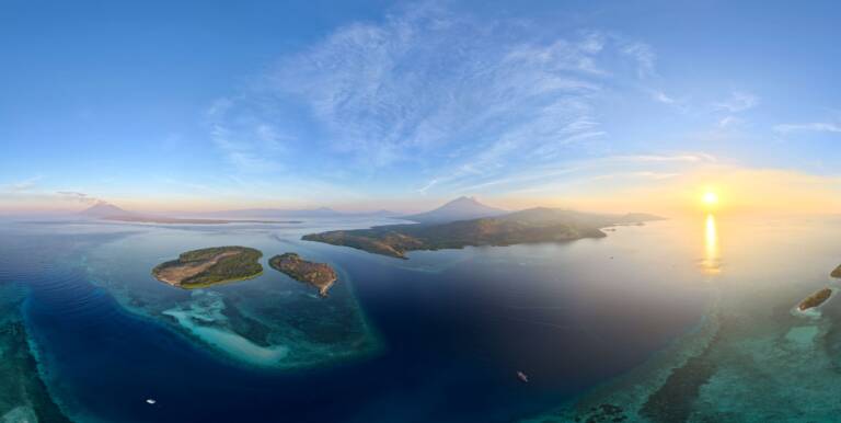 Aerial view at sunrise of reef-fringed islets with volcanoes on the horizon